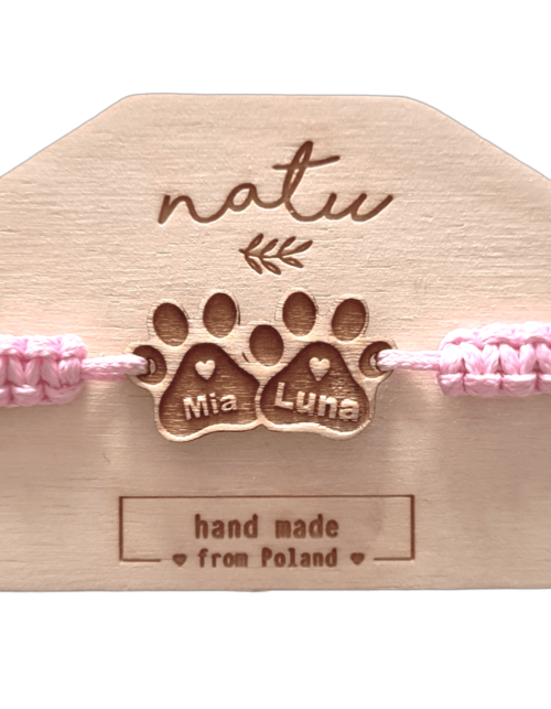 Bransoletka z drewnianą zawieszką przedstawiającą dwie łapki psa z grawerem imion piesków, na różowym, ręcznie plecionym sznurku.