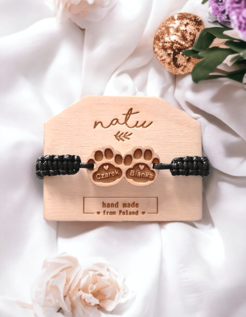 Bransoletka z drewnianą zawieszką przedstawiającą dwie kocie łapki z grawerem imion kotków, na czarnym, ręcznie plecionym sznurku.