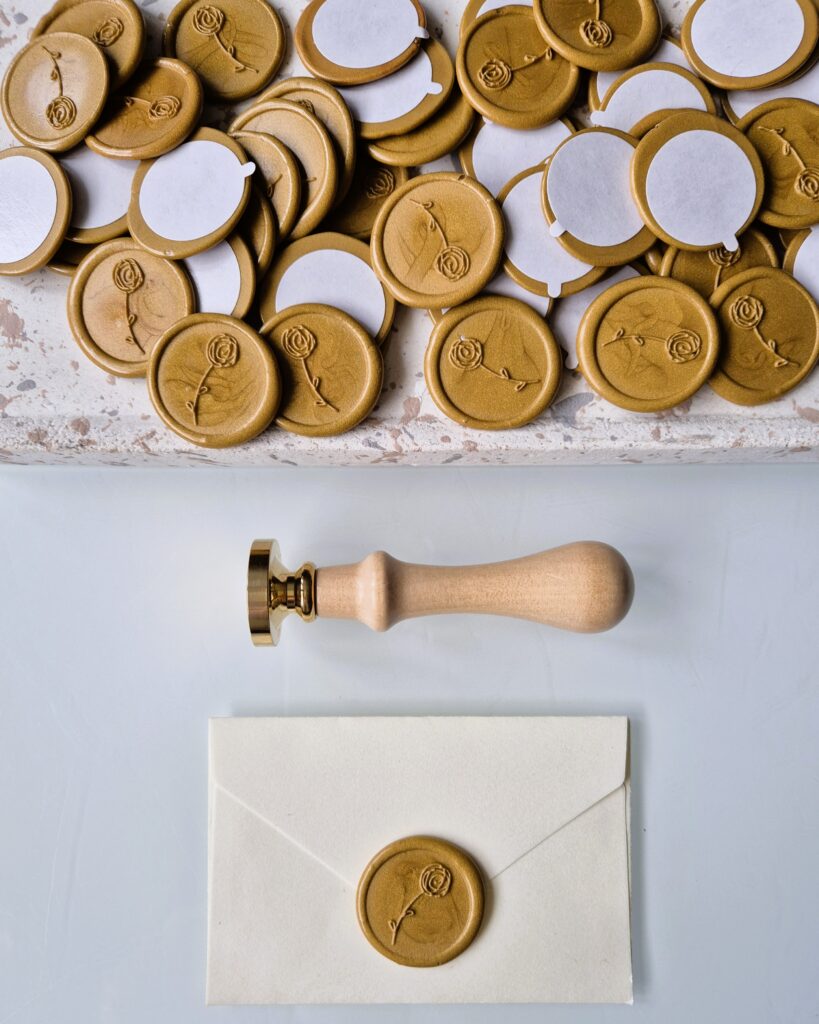 Złote gotowe odbicia lakowe z indywidualnym logo, wykonane przez Natu Artwork, z taśmą dwustronną do łatwego przyklejenia.